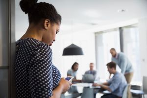Businesswoman texting cell phone outside conference room meeting