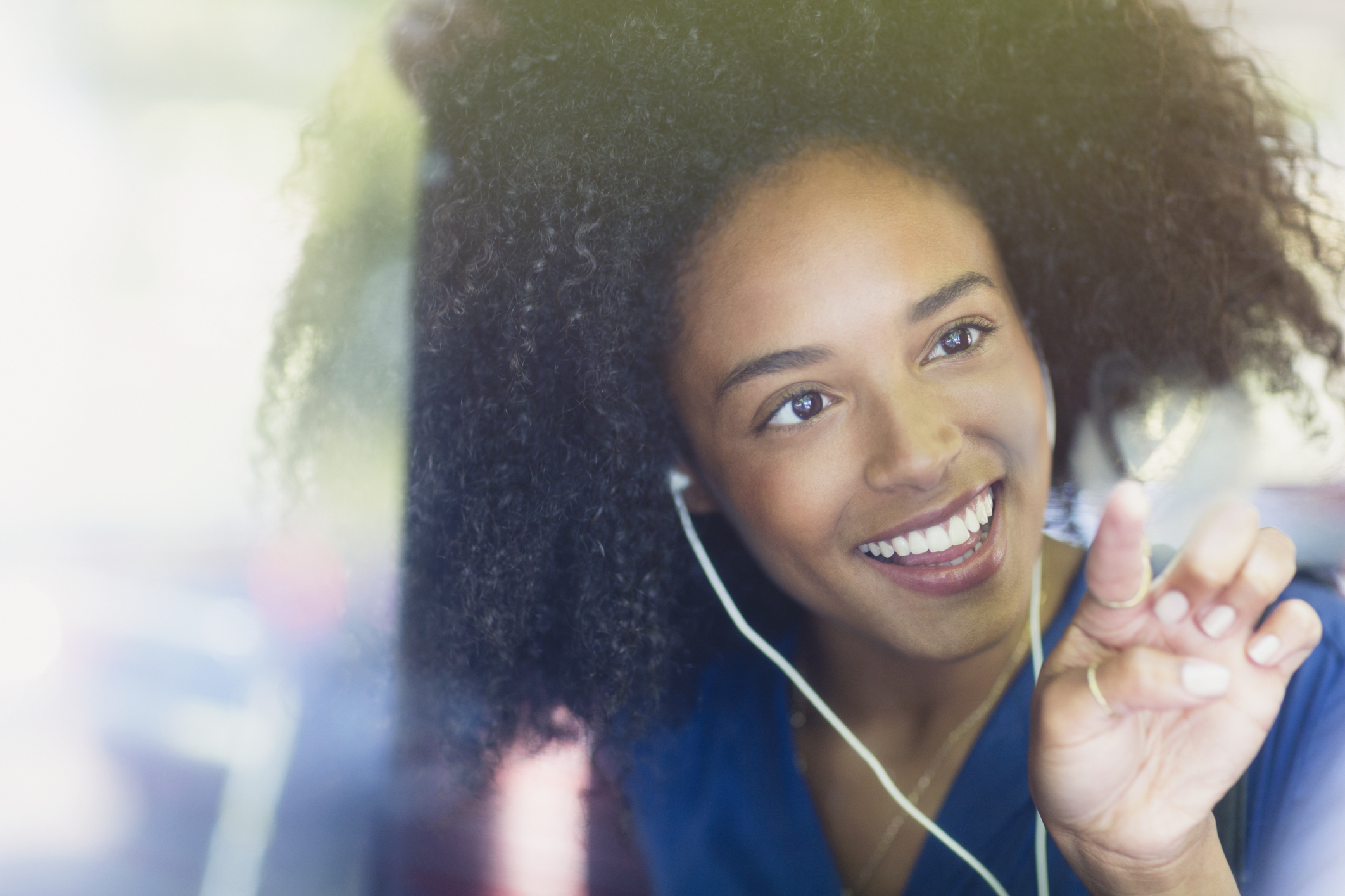 Smiling woman with afro and headphones drawing heart-shape on bus window