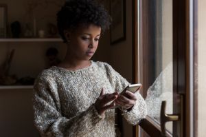 Young woman at the window looking at smartphone