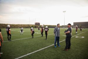 Coaches talking near teenage boy high school football team on football field