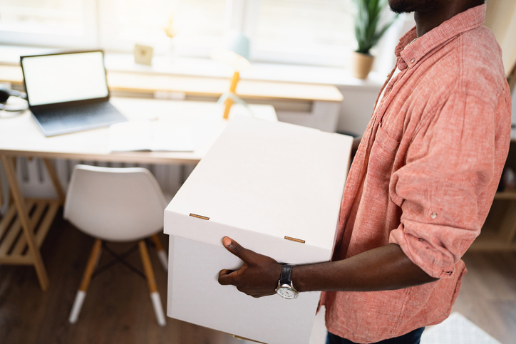 Unrecognizable male person of color carrying cardboard box