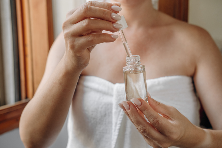 Women's hands with bottled moisturizing or anti-aging serum with dropper, daily skin care after a shower