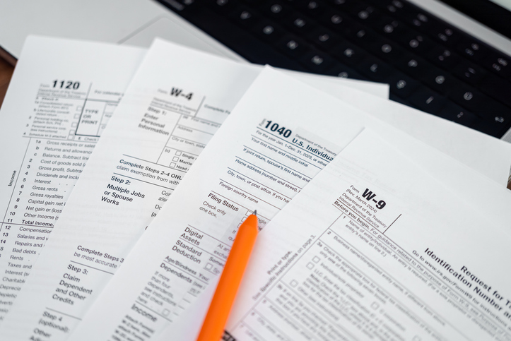 Tax forms and an orange pen on a wooden desk next to a laptop keyboard. Tax preparation, financial documentation, and accounting concept.