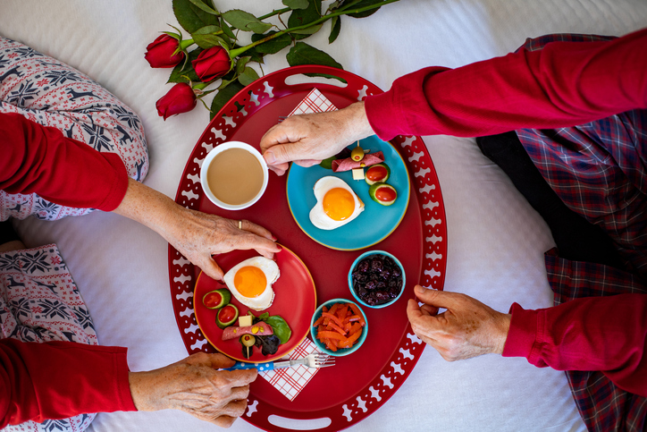 Valentine’s day surprise breakfast with heart shaped fried eggs, rose and gifts on the bed.